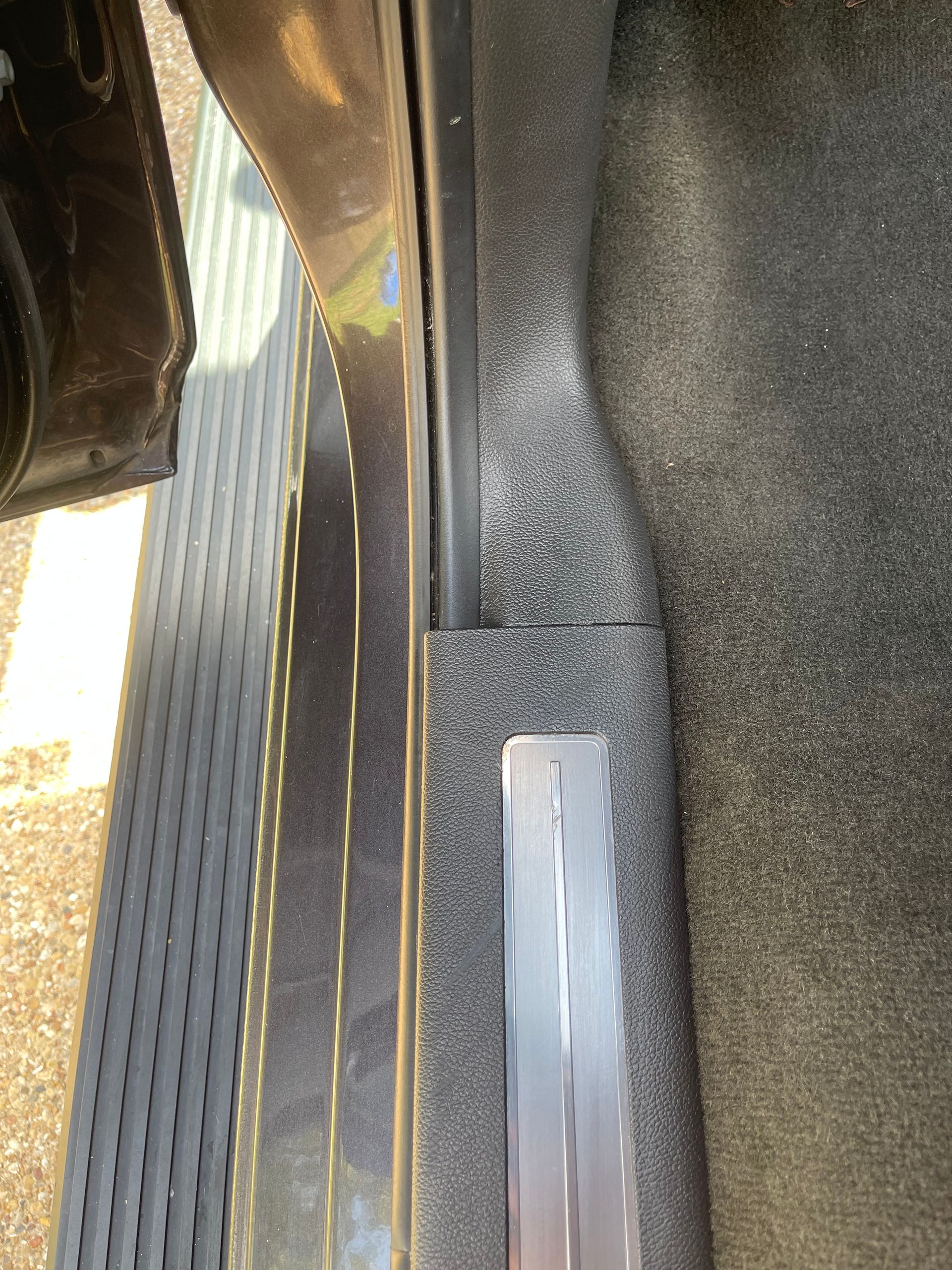 Door sill of a car interior with a dark gray plastic trim and metal plate.