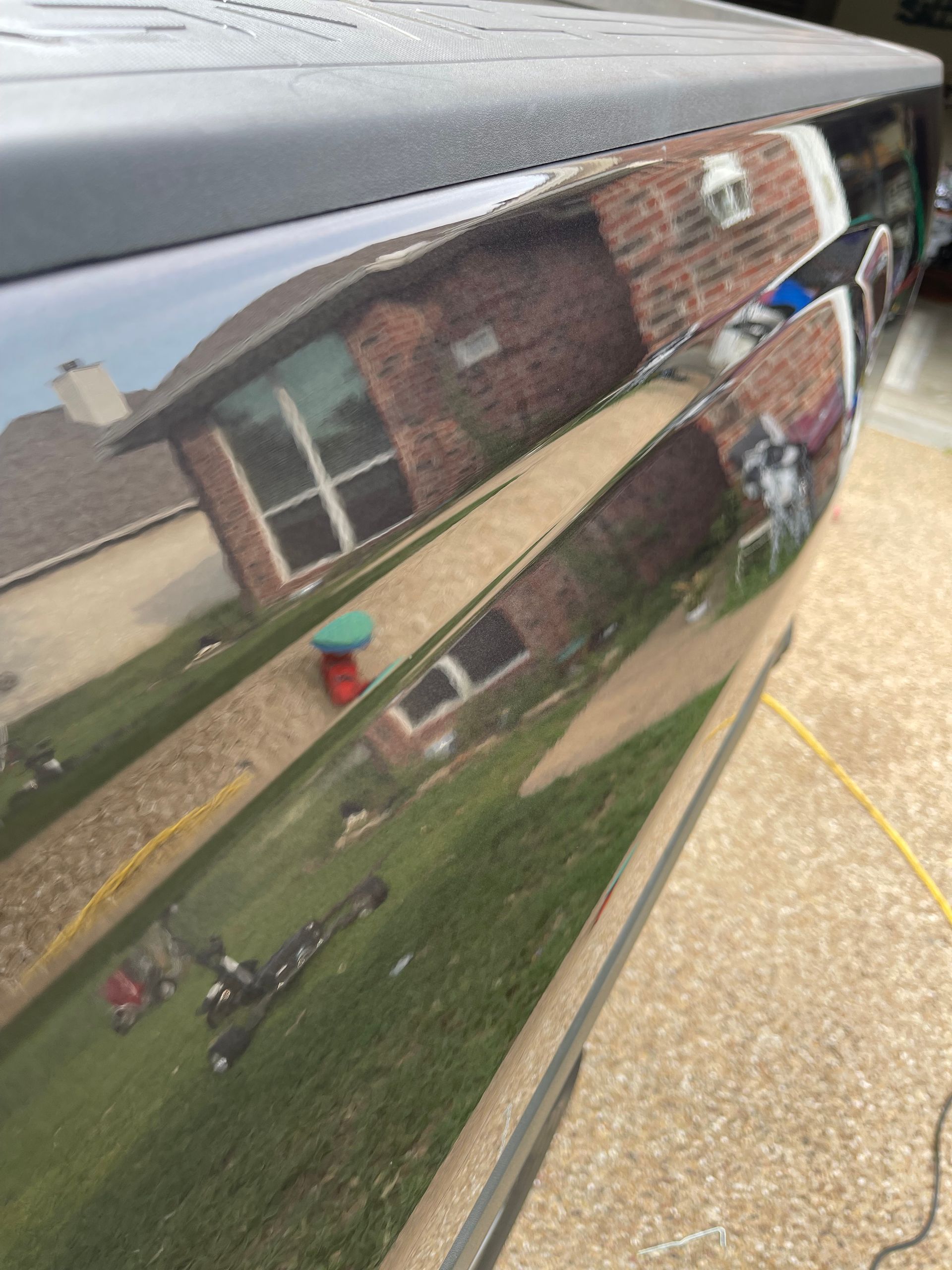 Reflective black car surface with house and yard visible in the reflection.