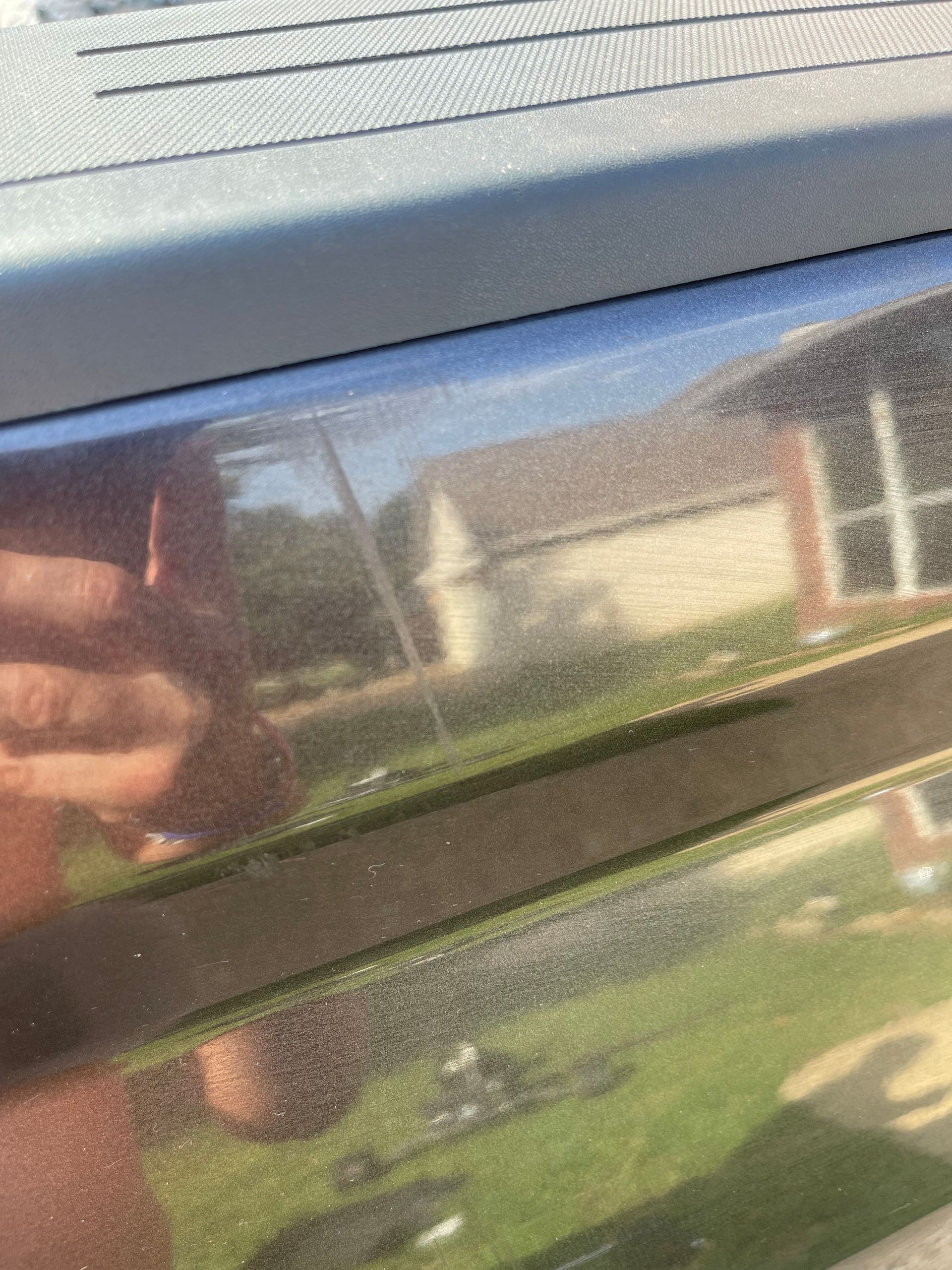 Close-up of a shiny, dark-colored car door with scratches, reflecting a house and yard.