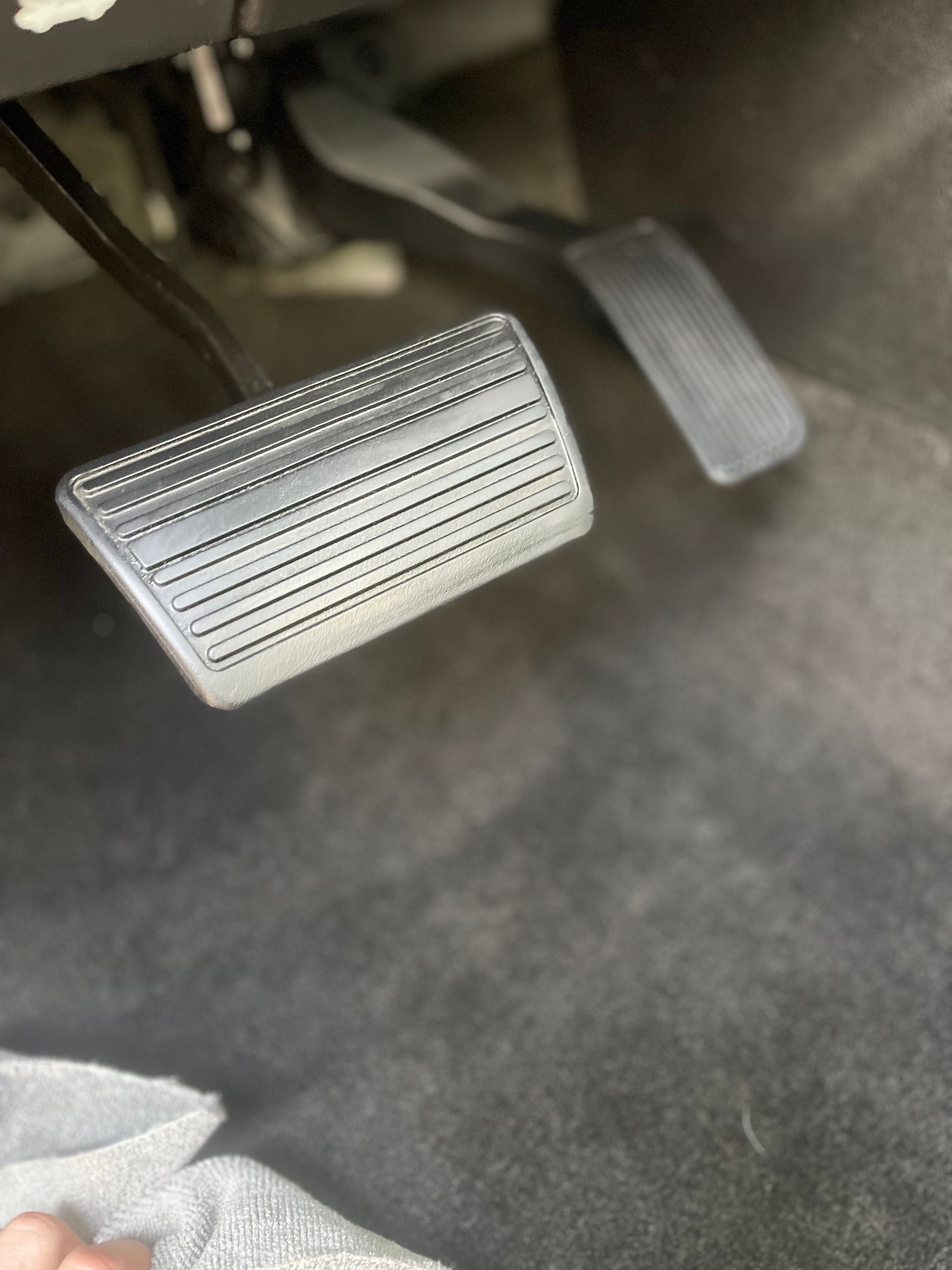 Car pedals: gas and brake. Black pedals on a gray carpeted floor.