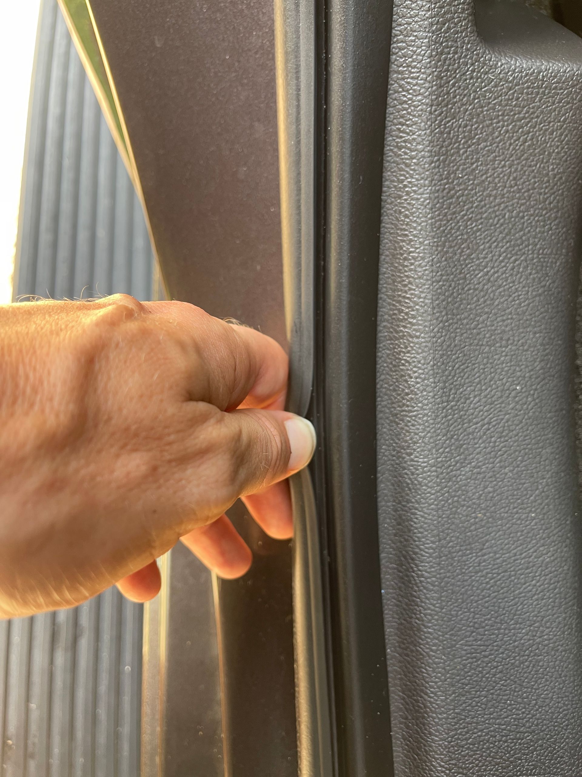 Hand touching a black rubber seal around a car door, suggesting a potential leak.
