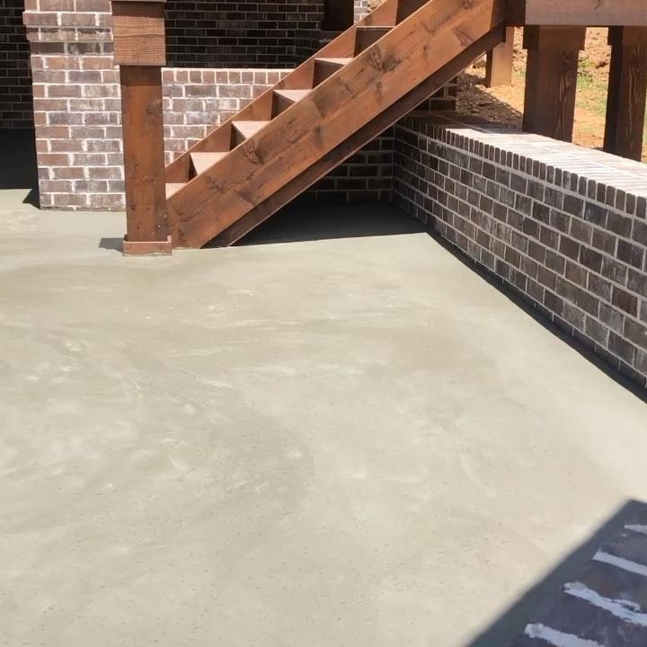 A concrete patio with a brick wall and wooden stairs leading up.