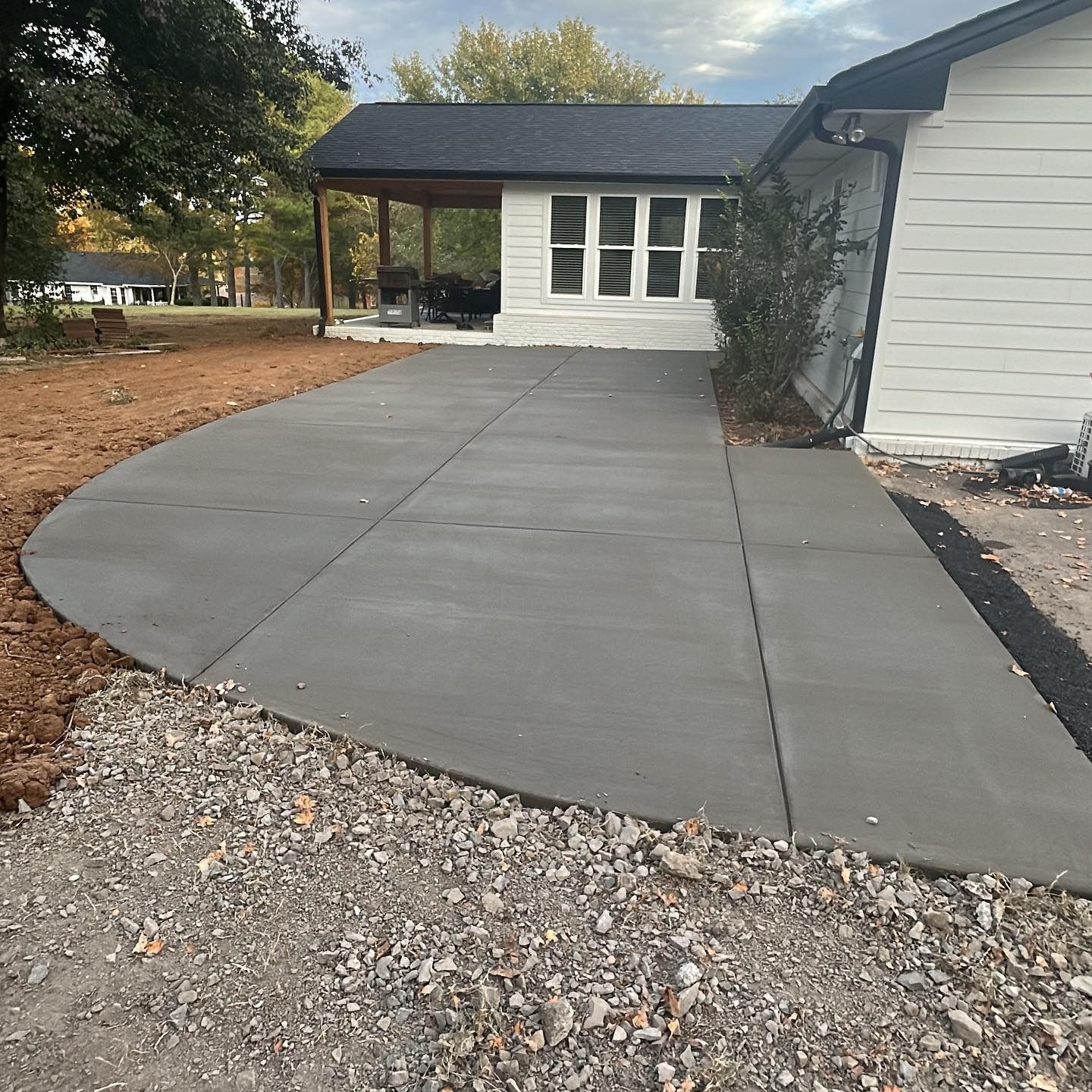 Newly poured gray concrete driveway curving towards a white house with a covered porch.