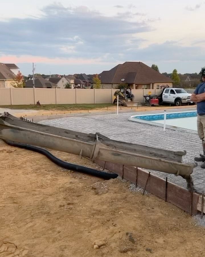 Construction site with pool, concrete forms, and equipment. A worker stands nearby.