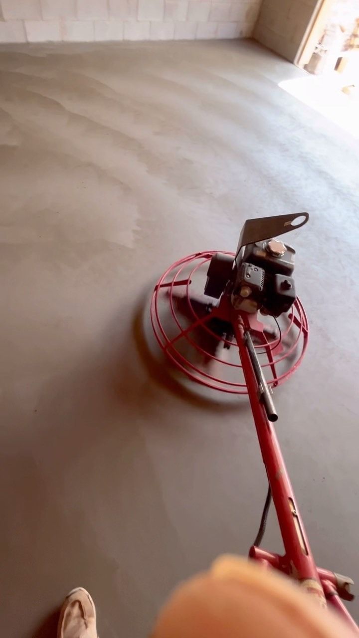 Person using a red power trowel on a freshly poured concrete floor.