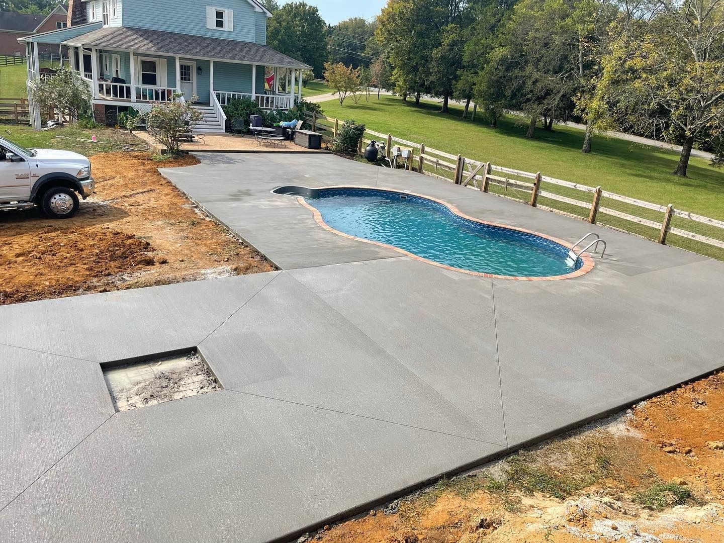 Concrete pool deck with pool, house in background, truck on left, and fence on right.