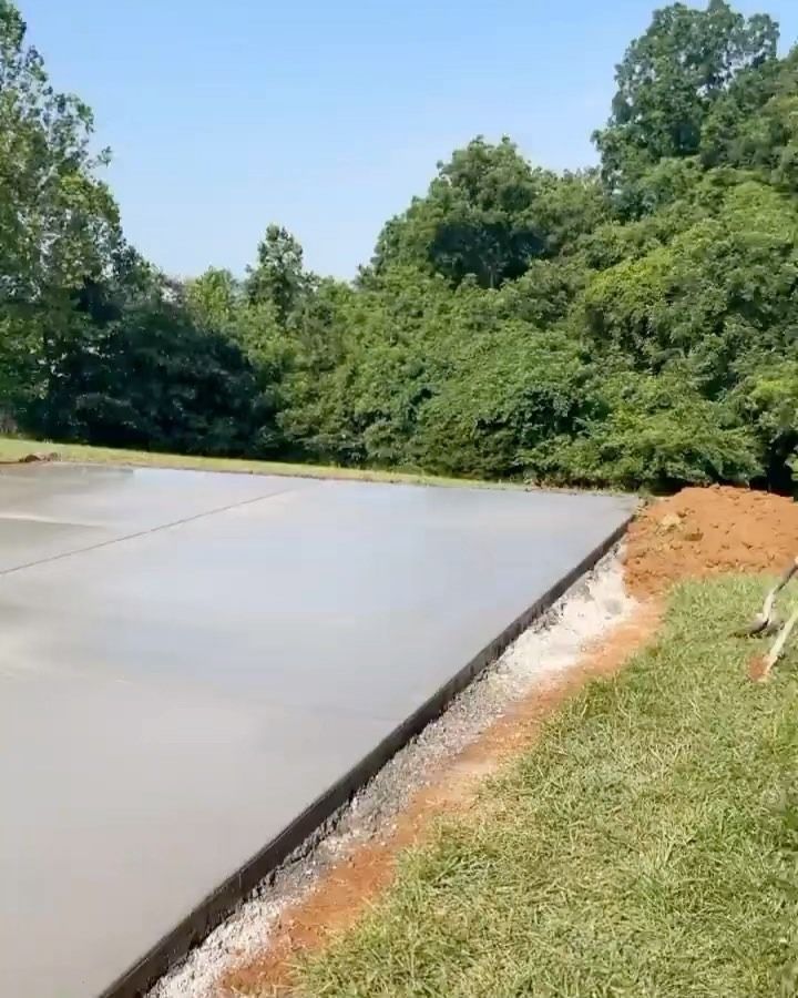 Freshly poured concrete slab in a grassy yard, with a treeline in the background.