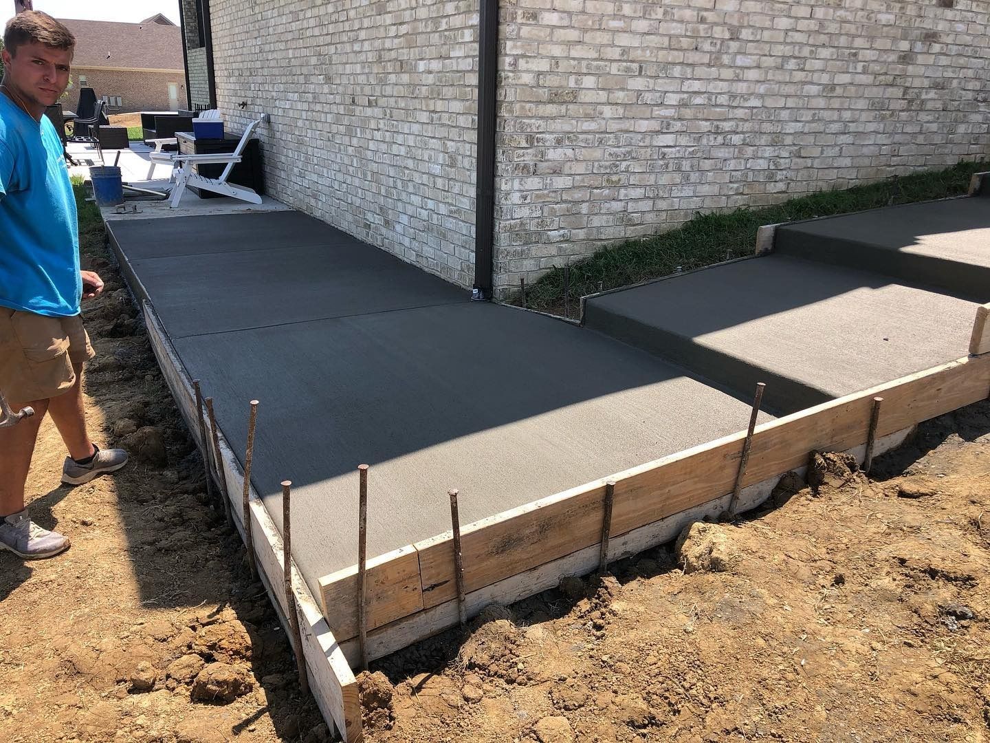 Freshly poured concrete walkway with forms; a person stands nearby.