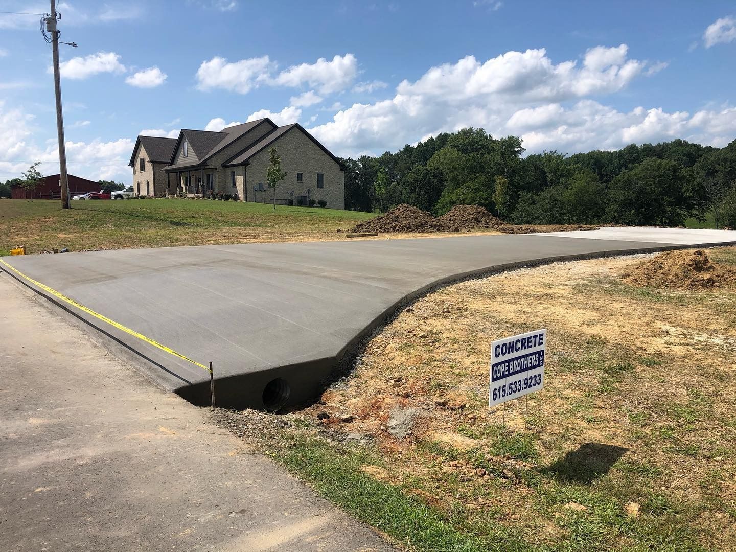 Newly poured concrete driveway with a house in the background and a drainage ditch.