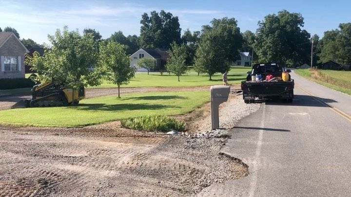A black truck parked on a road next to a mailbox. Trees and houses are in the background on a sunny day.