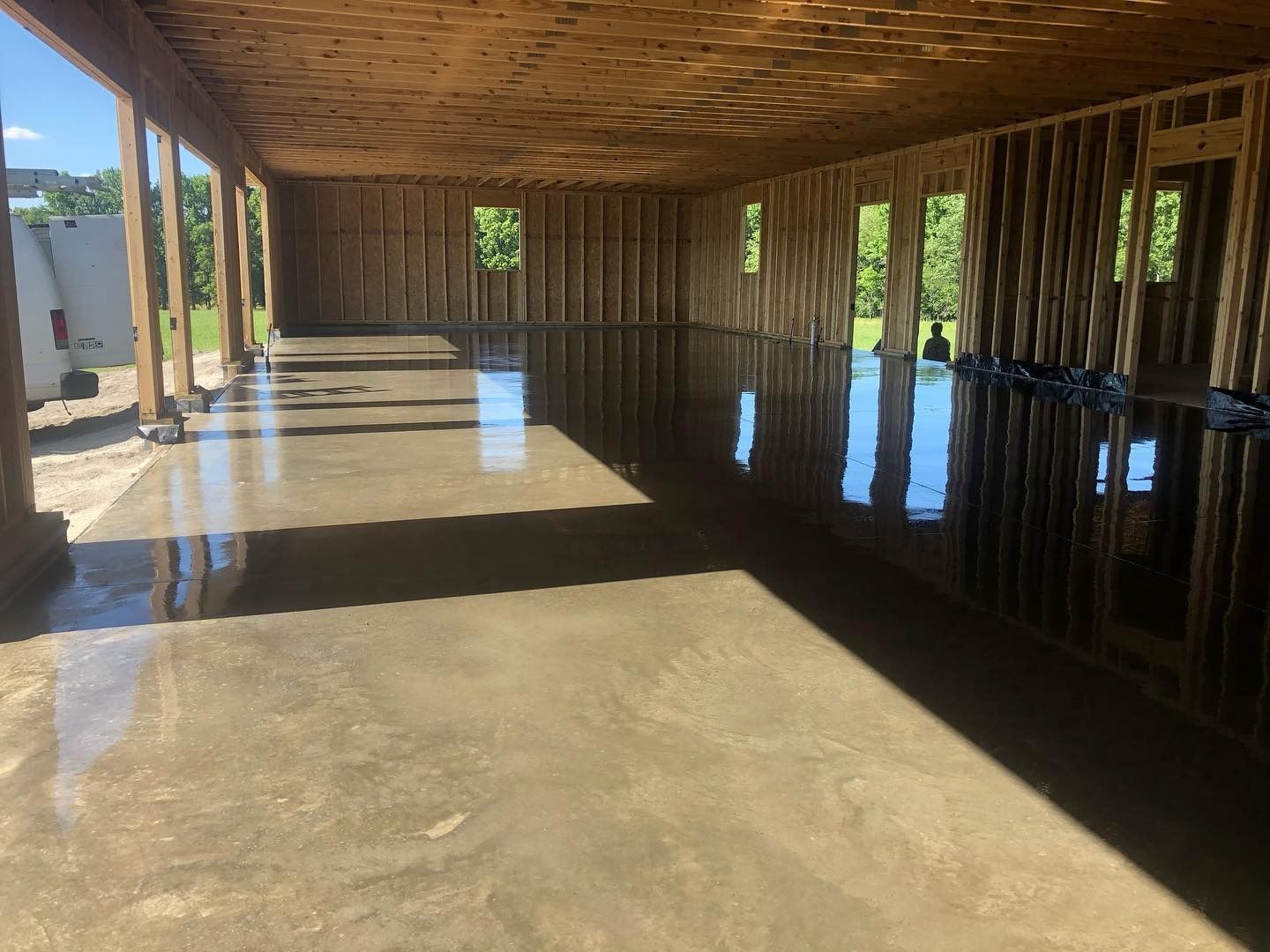 Interior of a building under construction with a shiny, wet concrete floor reflecting the sunlight.