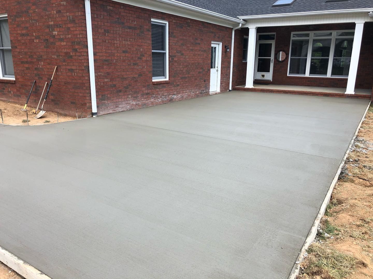 Newly poured gray concrete patio next to a red brick house.