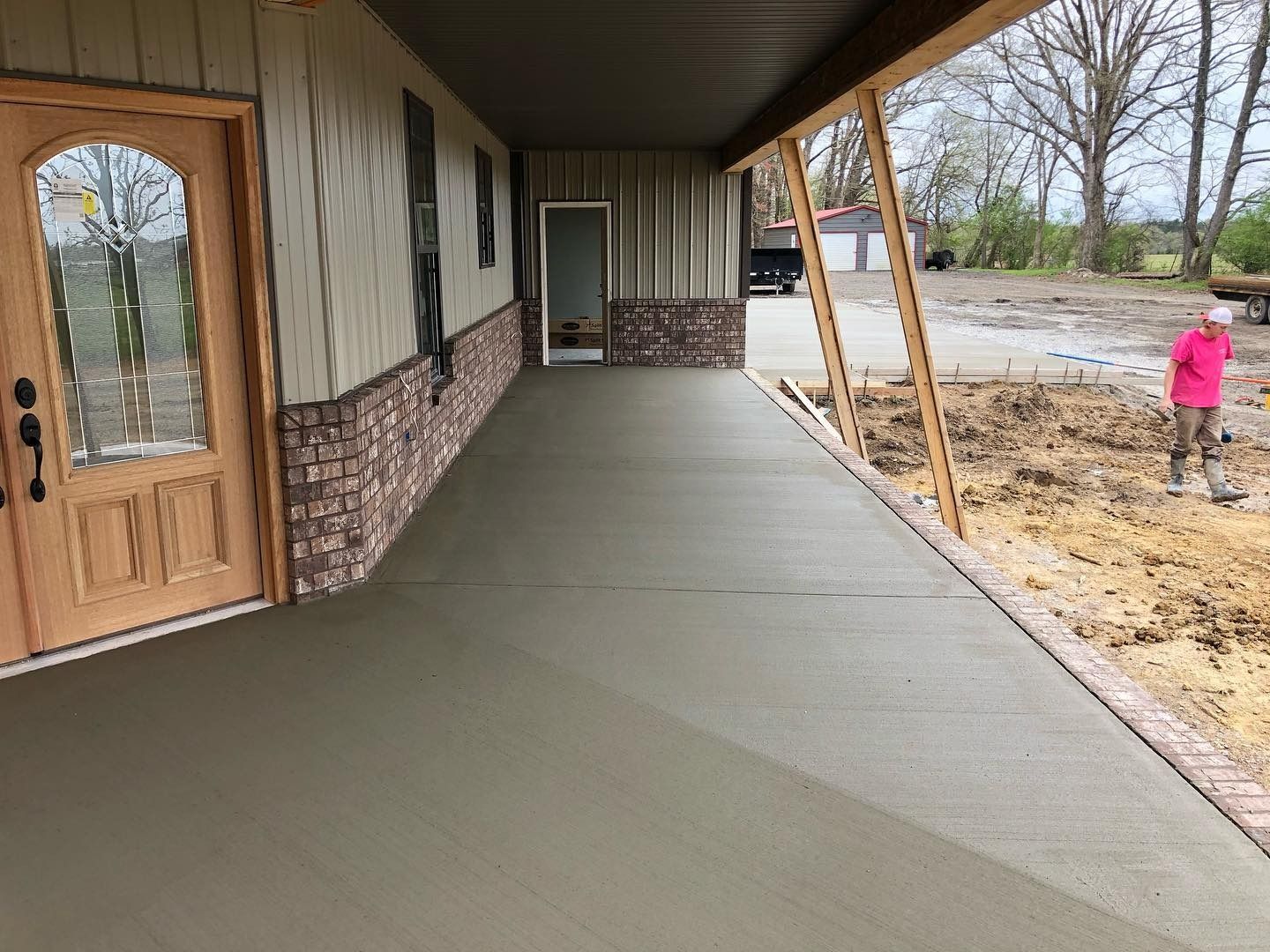 Newly poured concrete porch with brick accents, person working in background.