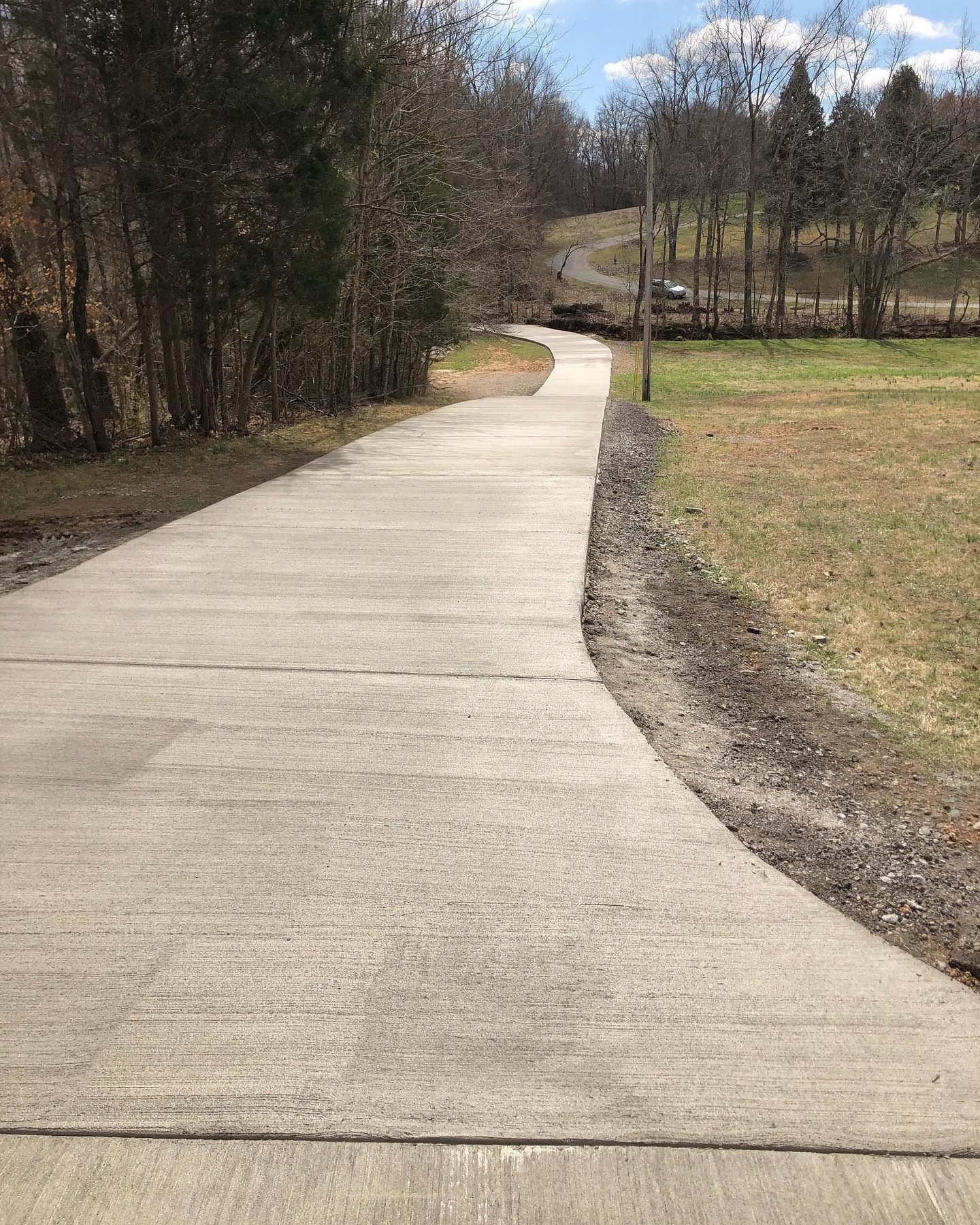 Concrete path curves through a grassy area and trees on a sunny day.