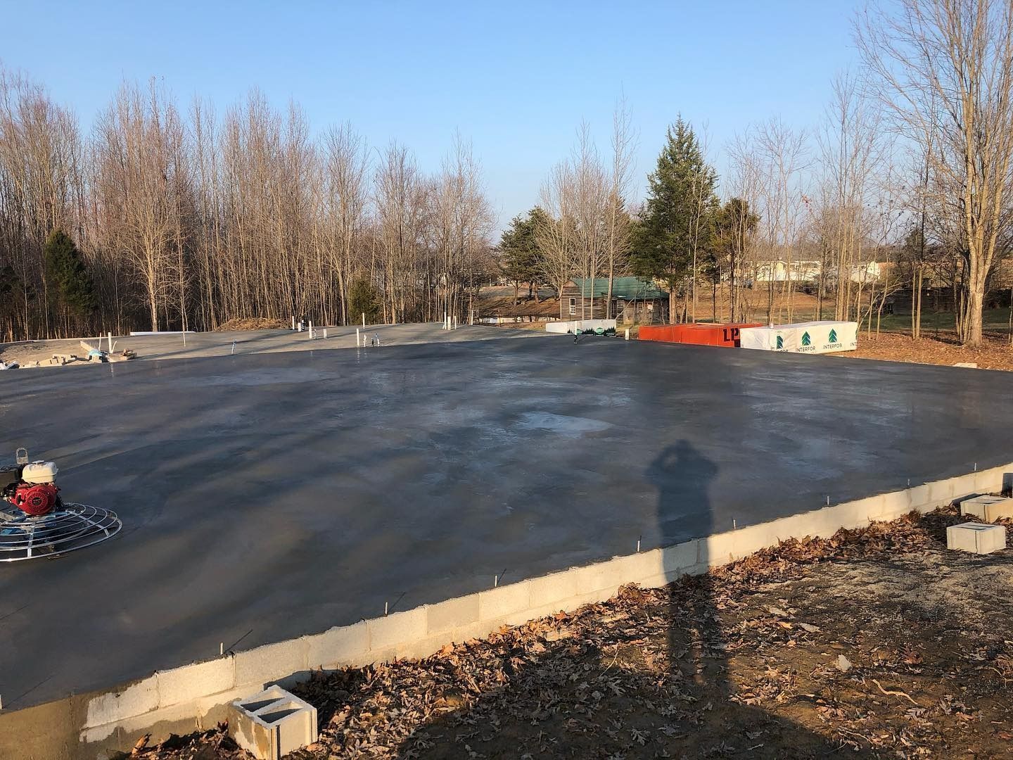 Newly poured concrete foundation. Construction site with trees in the background. Sunny day.