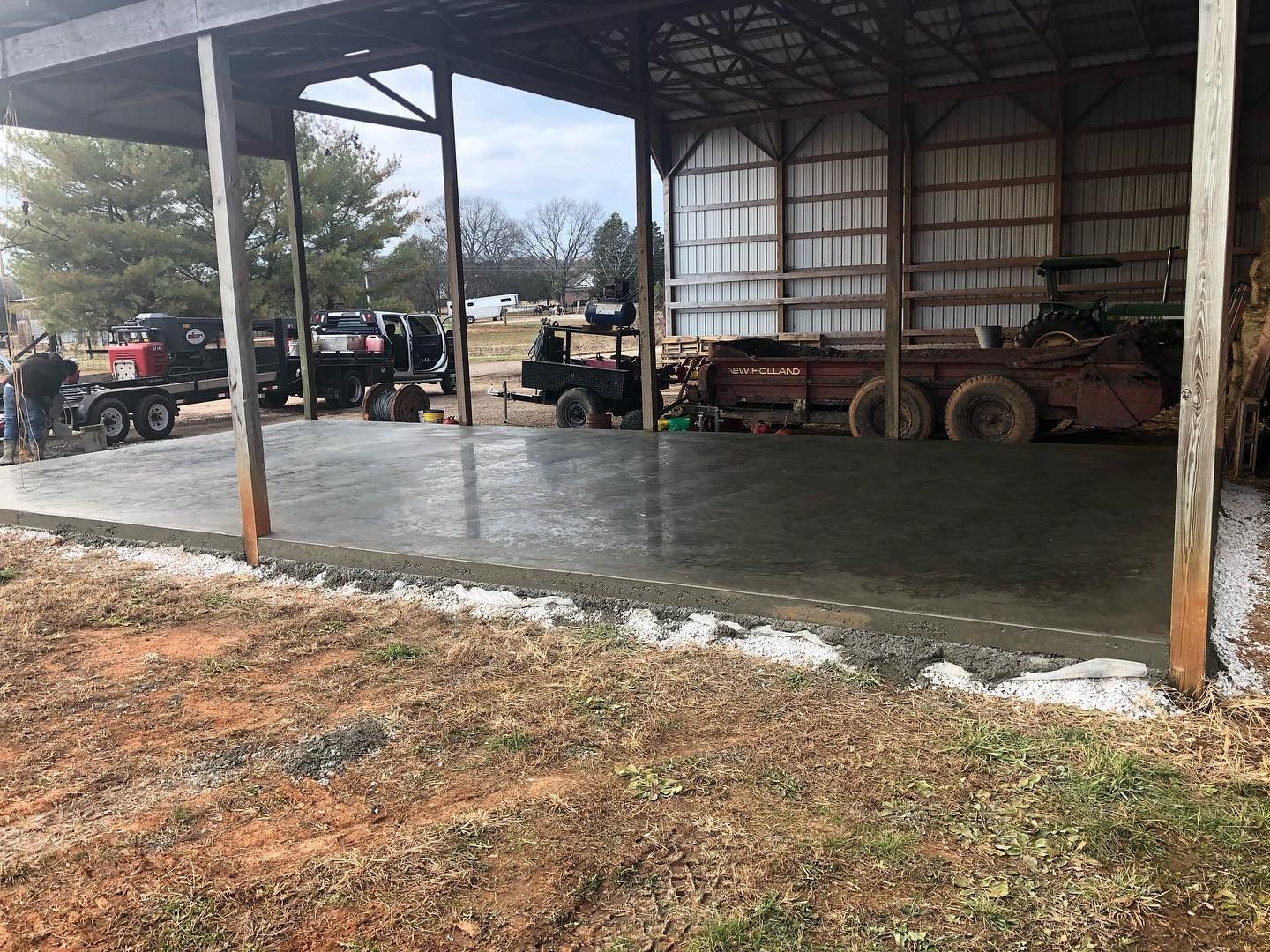 New concrete floor under a barn roof, outside. Several vehicles and people are nearby.