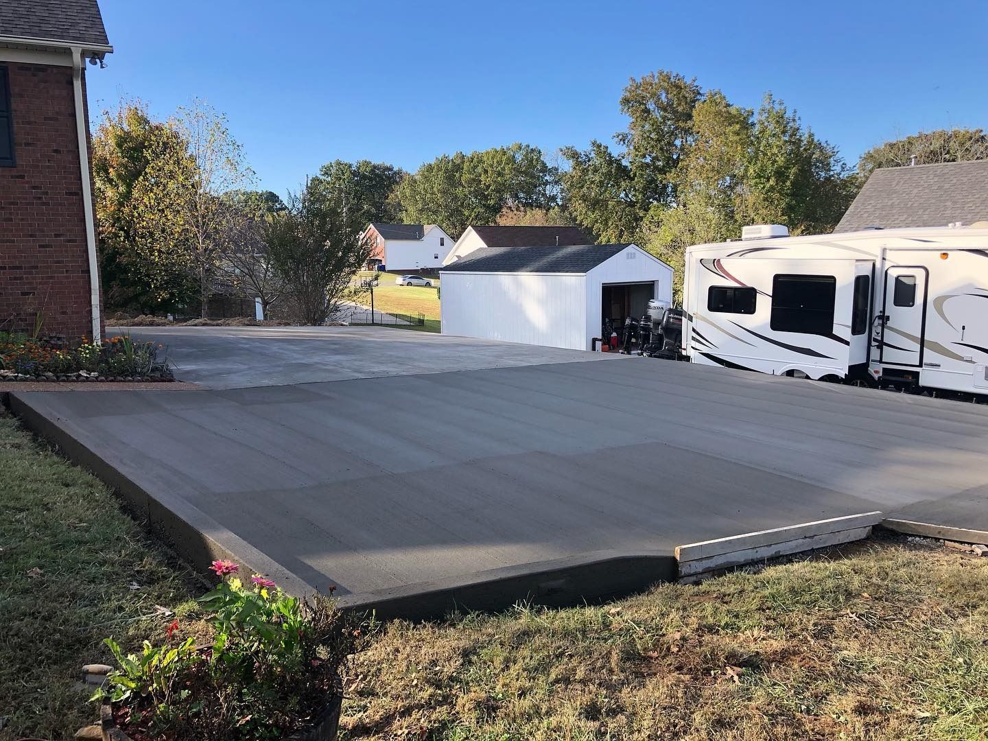 Newly poured concrete driveway with RV parked to the right; small garage in the background.