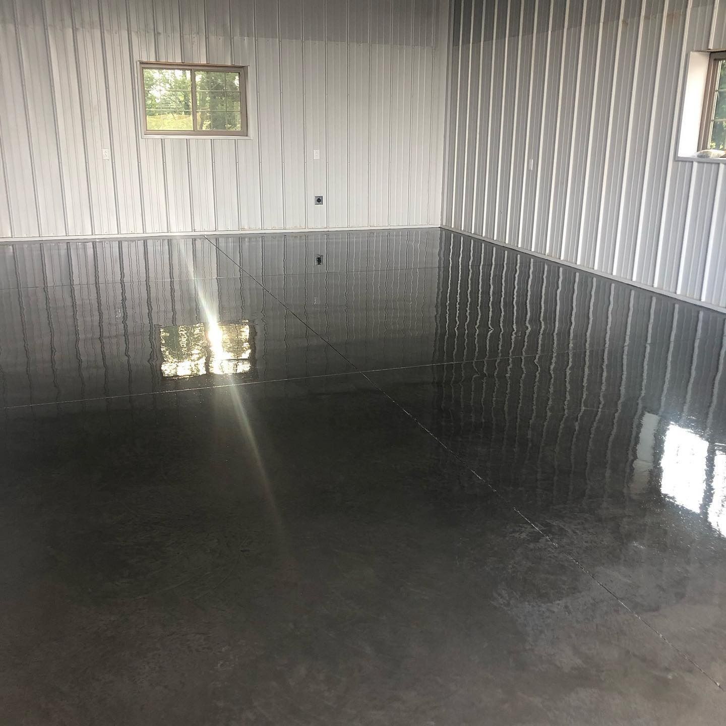Interior of a metal building with a dark, glossy epoxy floor reflecting the windows and walls.