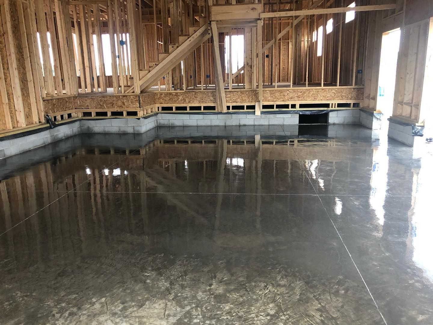Interior of a building under construction, with a wet, reflective concrete floor. Wooden framing is visible.