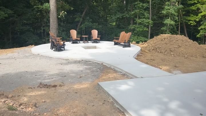 Outdoor concrete patio with fire pit and chairs, surrounded by trees.