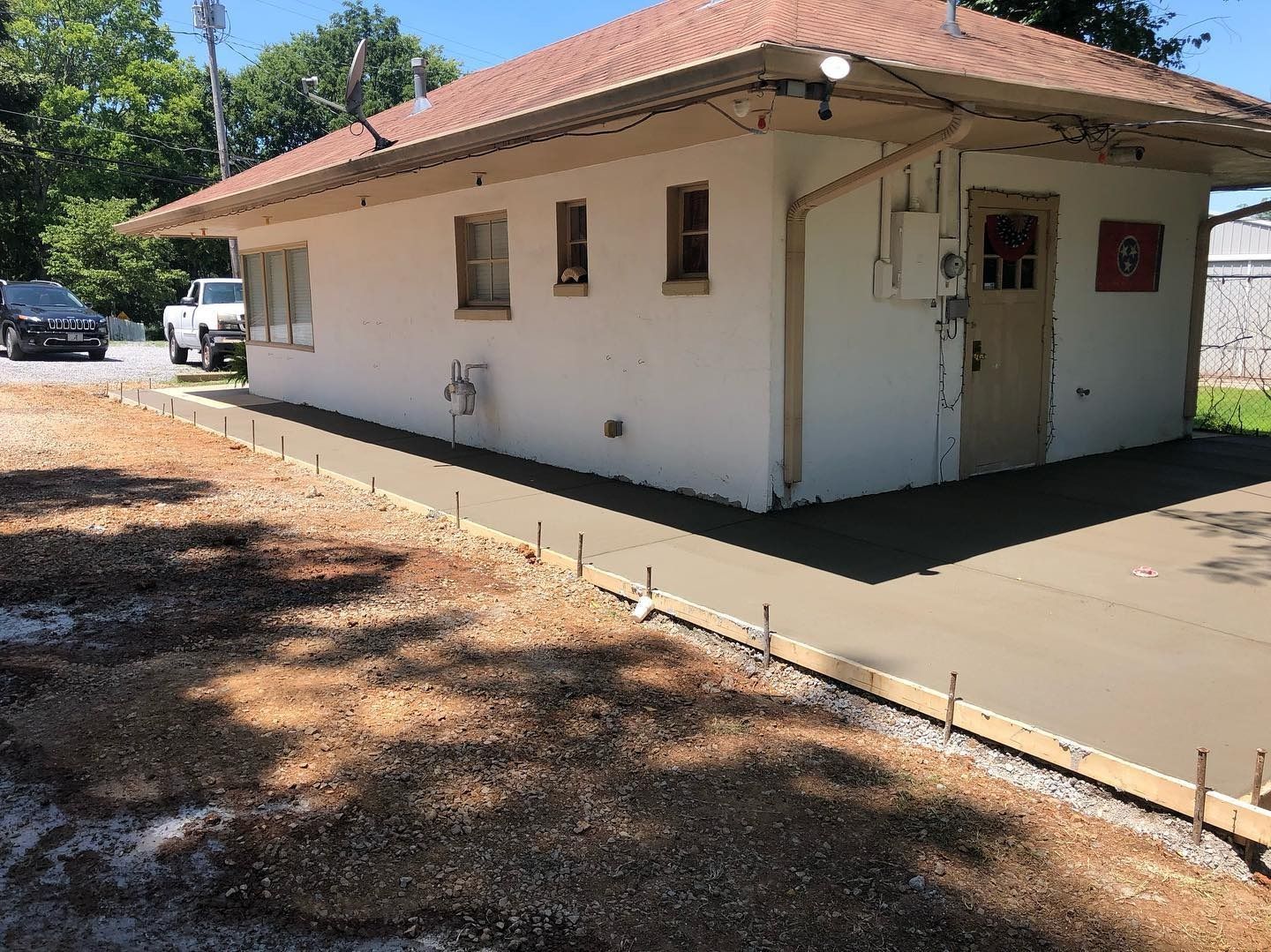 Building with newly poured concrete walkway. Gravel and car visible.
