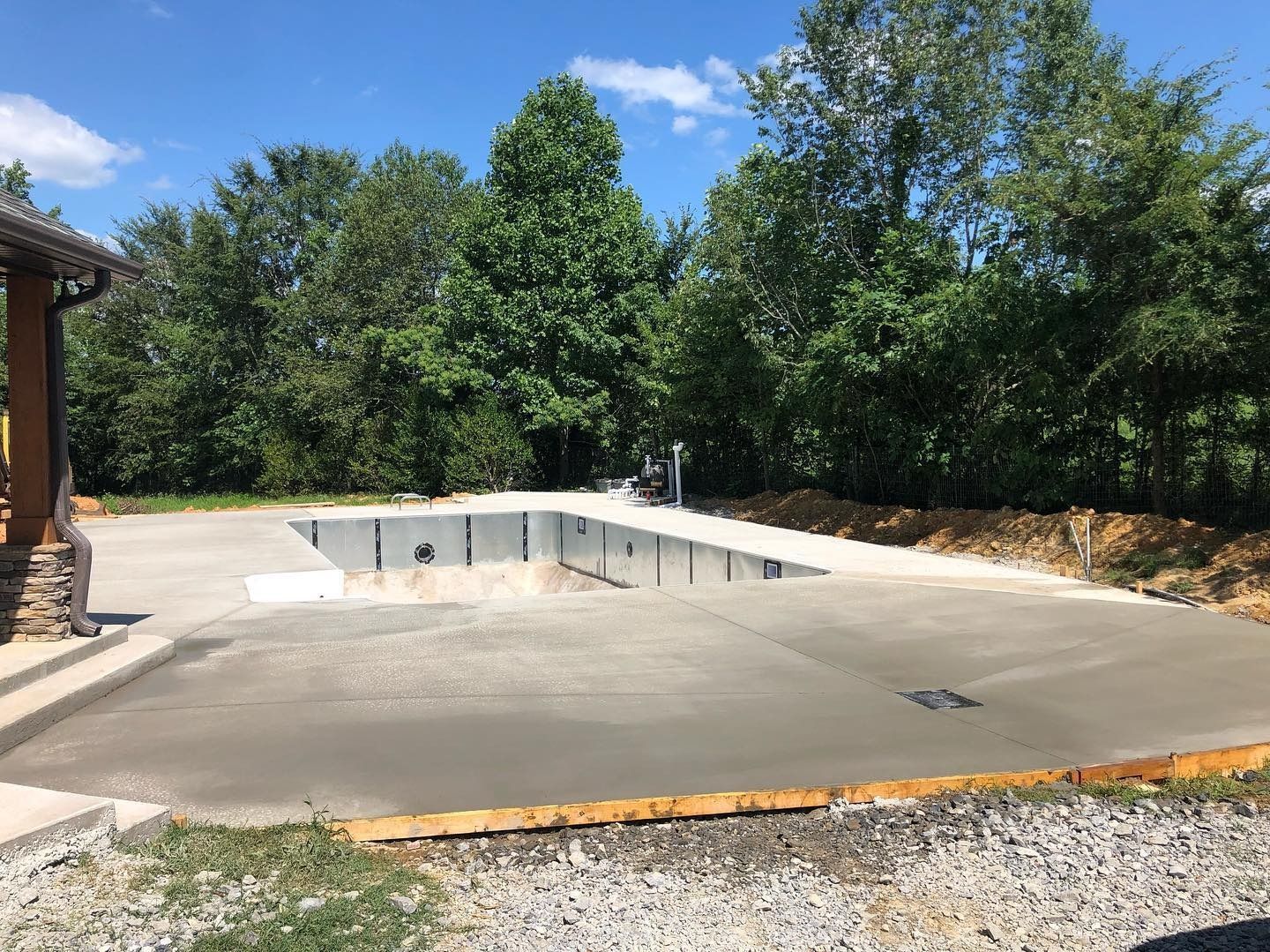 Concrete pool construction with surrounding concrete, gravel, and trees.