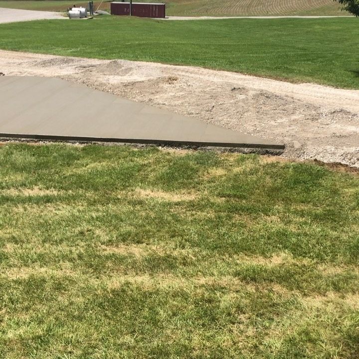 Freshly poured concrete driveway with a gravel border, next to a grassy area.