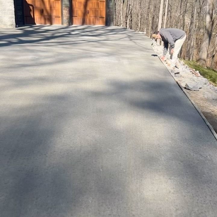 Person working on the edge of a newly poured concrete driveway; wooden garage doors in background.