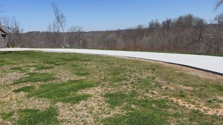 A paved path curves through a grassy area, leading toward trees and a blue sky.