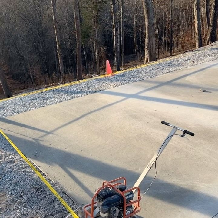 Concrete slab being finished with a power tool, forest in background, caution tape on the edge.