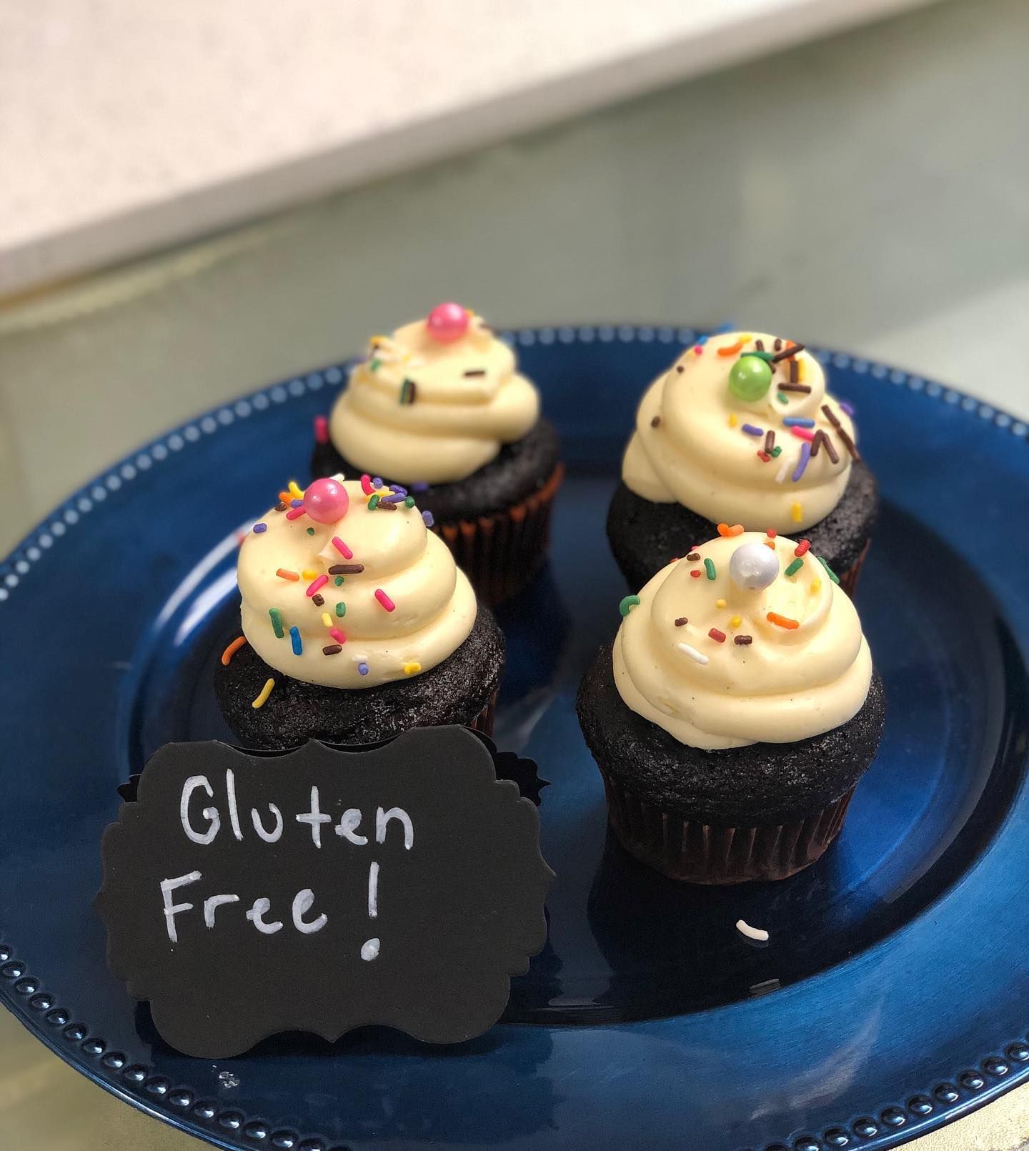 Four cupcakes on a blue plate with a sign that says gluten free