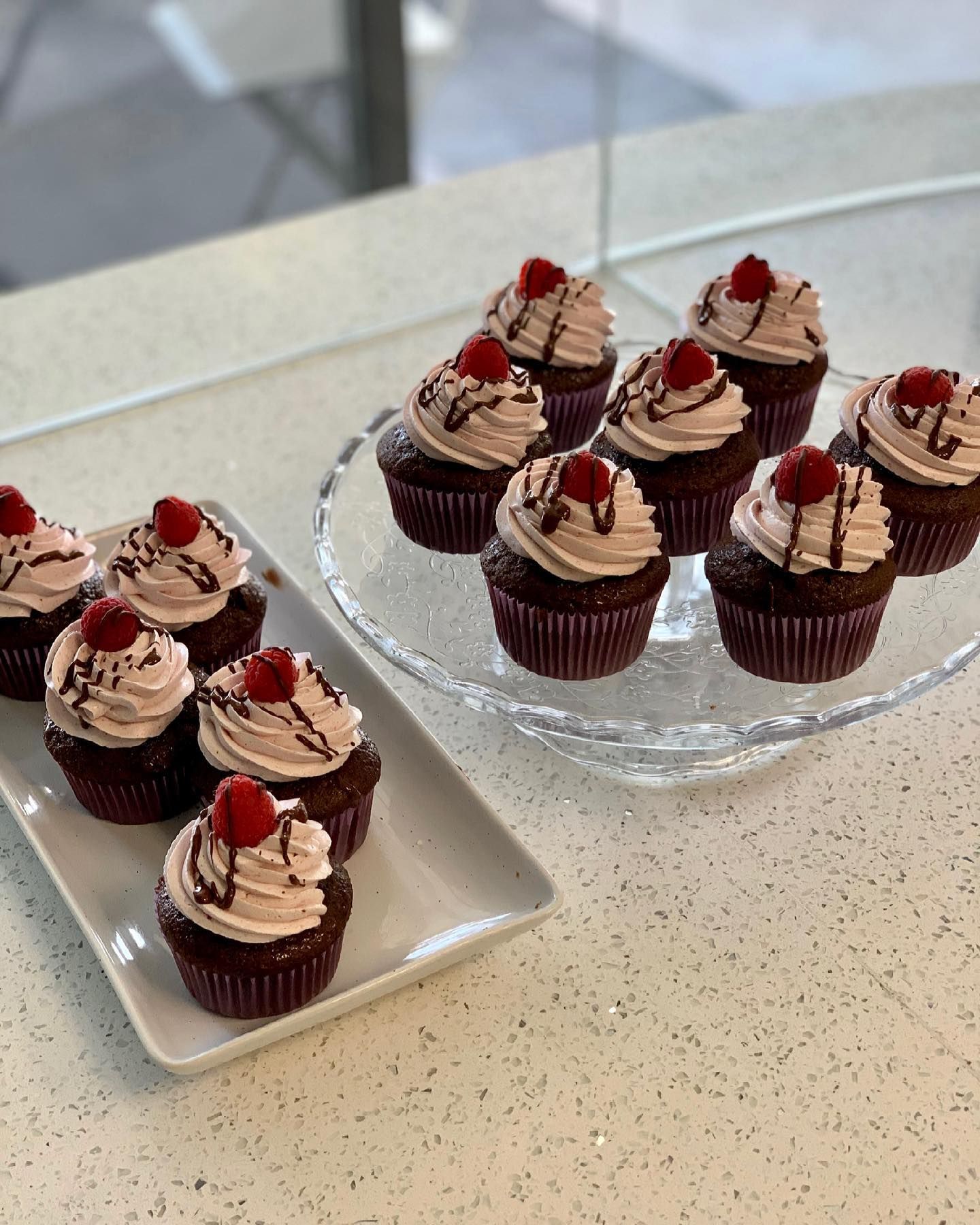A tray of cupcakes on a table next to a glass plate of cupcakes.