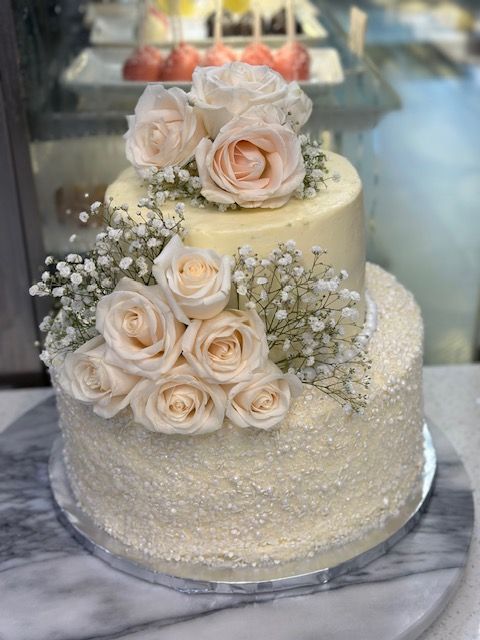 A white wedding cake with roses and baby 's breath on top.