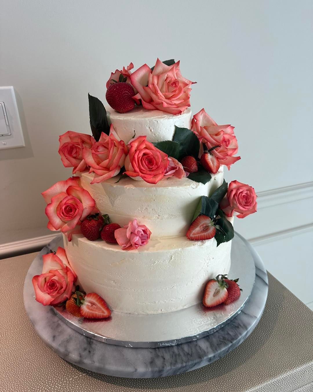 A three tiered cake with pink roses and strawberries on top.
