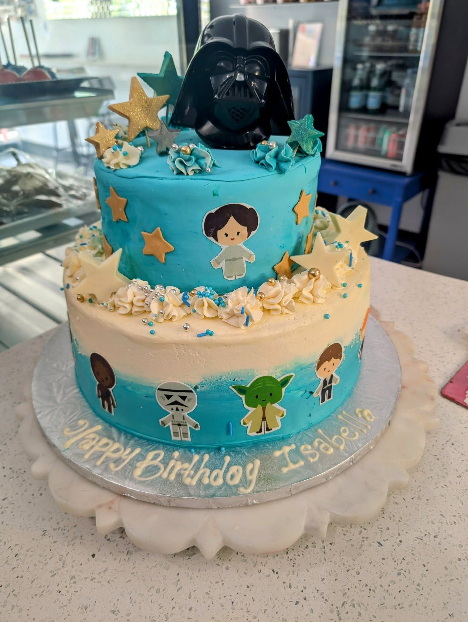 A birthday cake with a darth vader and yoda on it is sitting on a table.