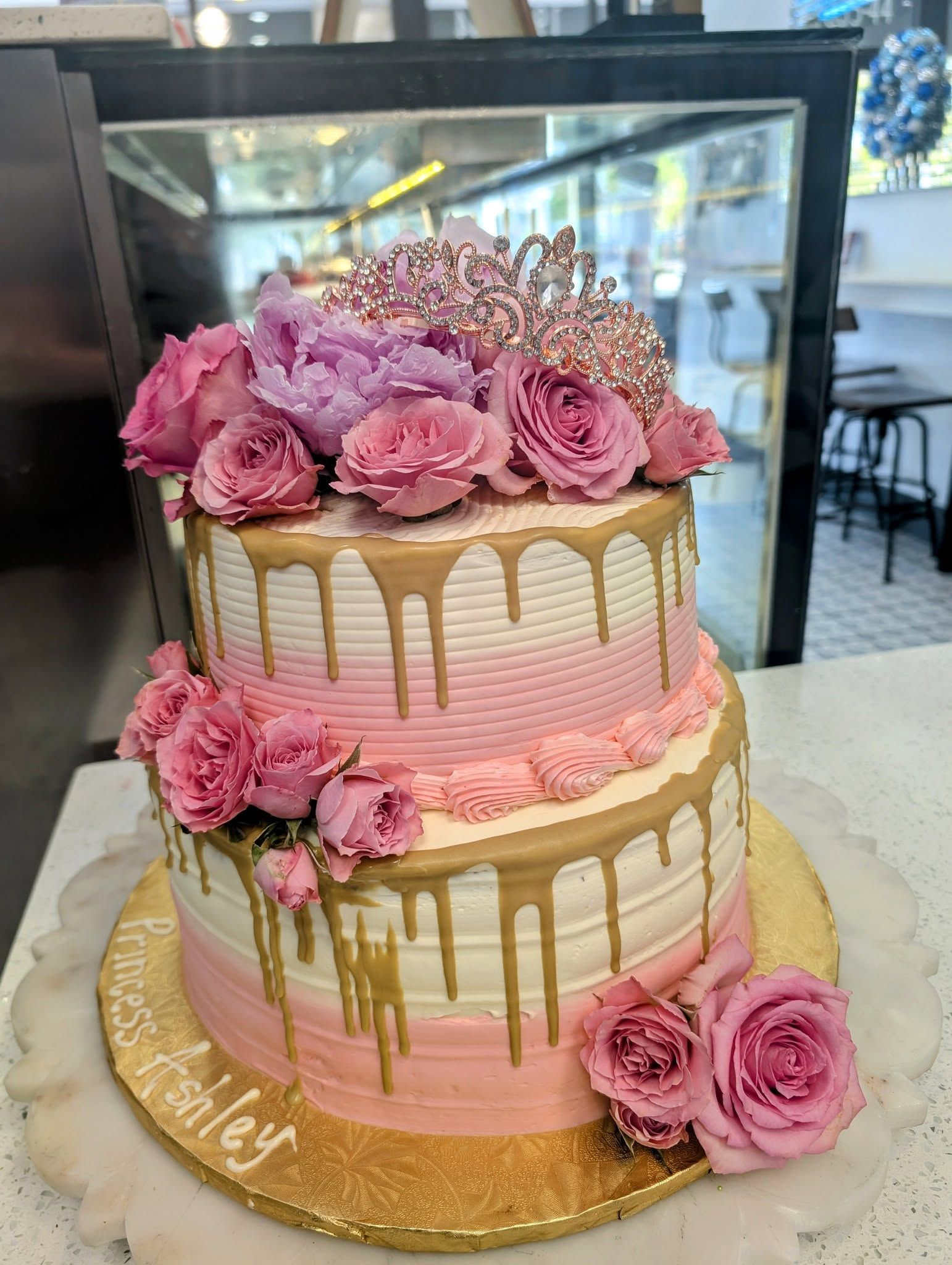 A pink and gold birthday cake with flowers on top is sitting on a table.