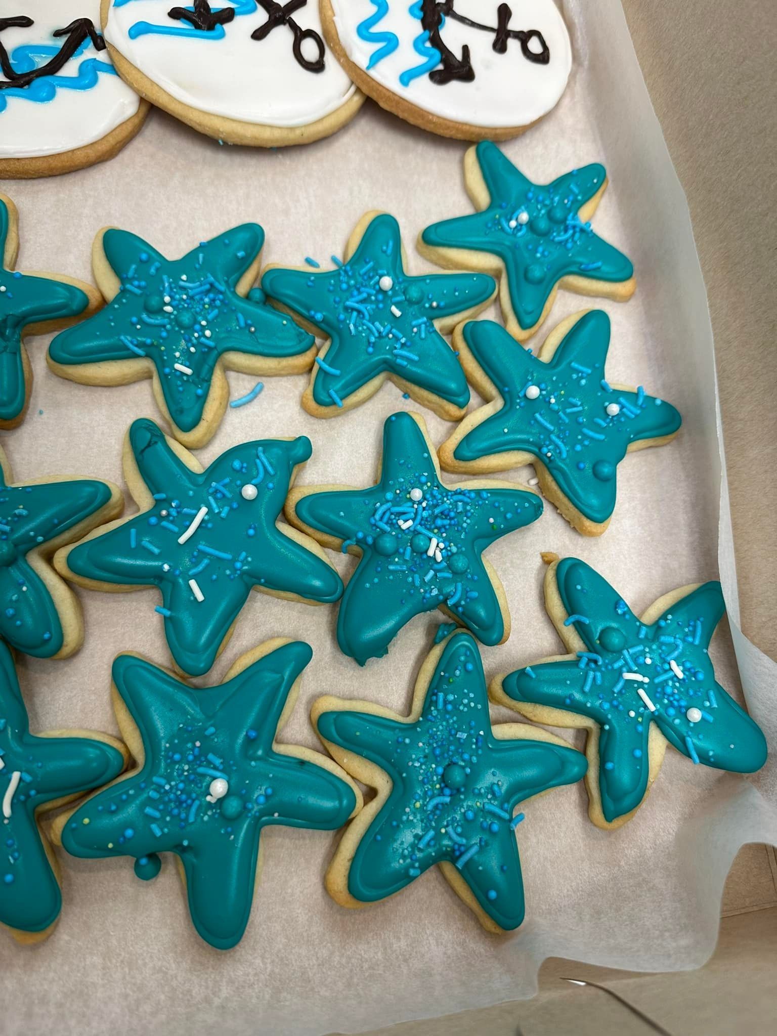 A box of starfish shaped cookies with blue frosting and sprinkles