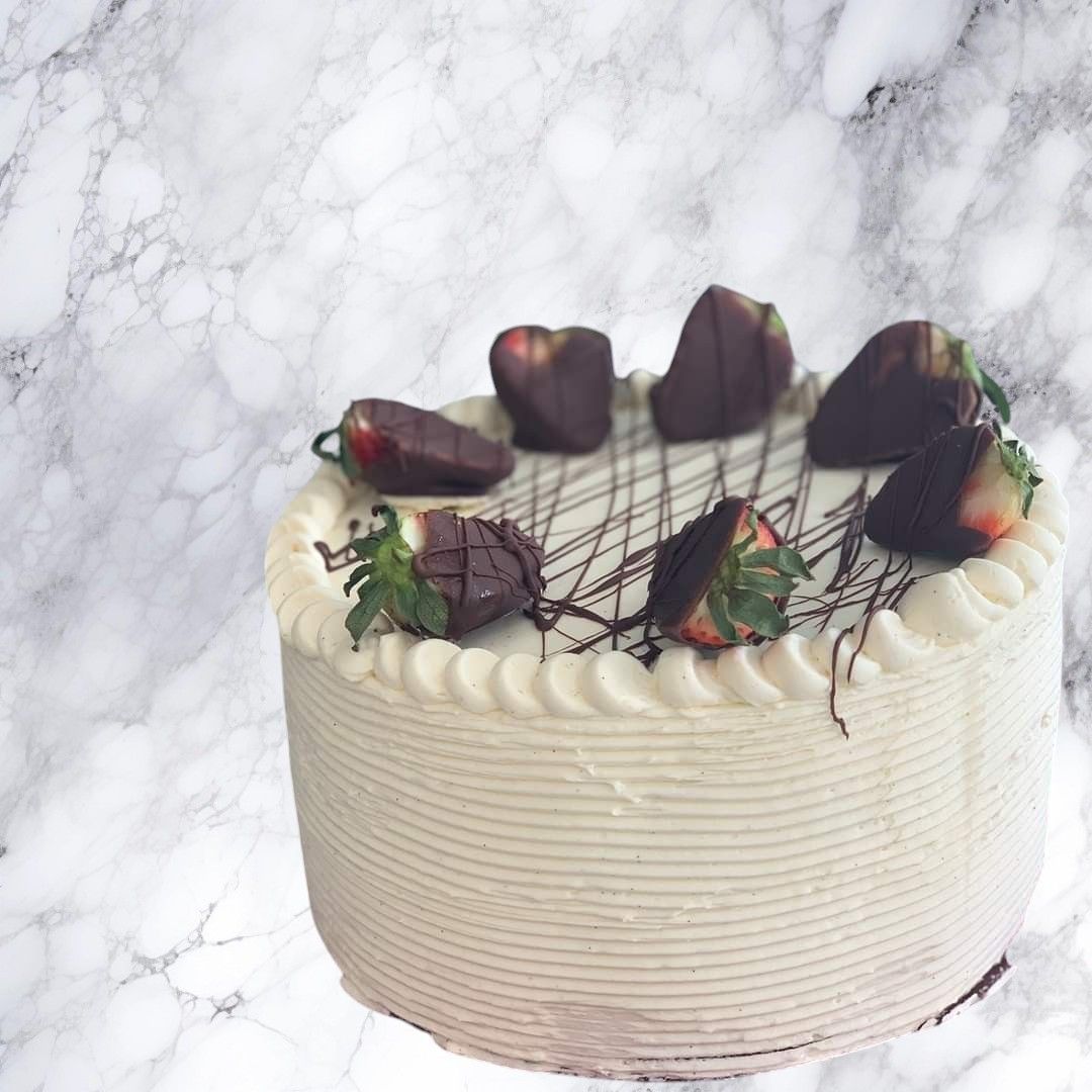 A white cake with chocolate strawberries on top