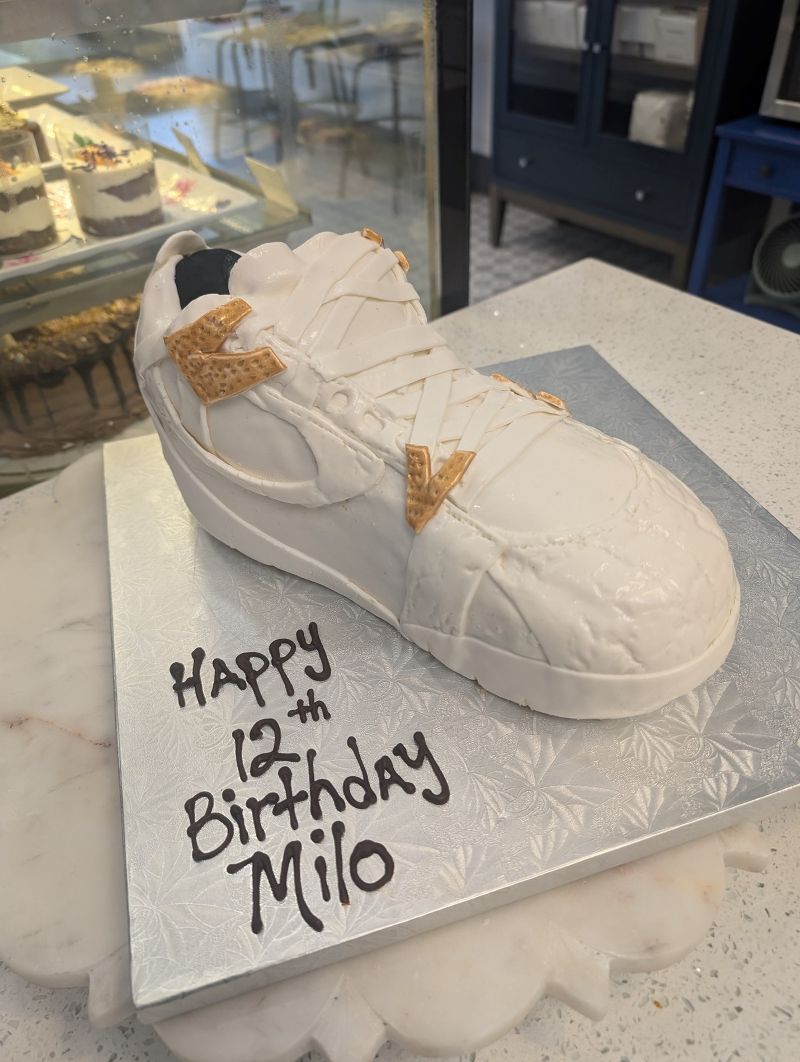 A cake in the shape of a shoe with the words happy 12th birthday milo written on it