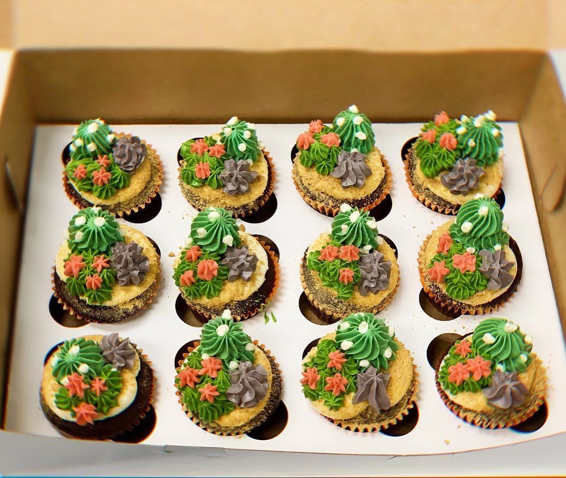 A box of cupcakes with green frosting and flowers on them