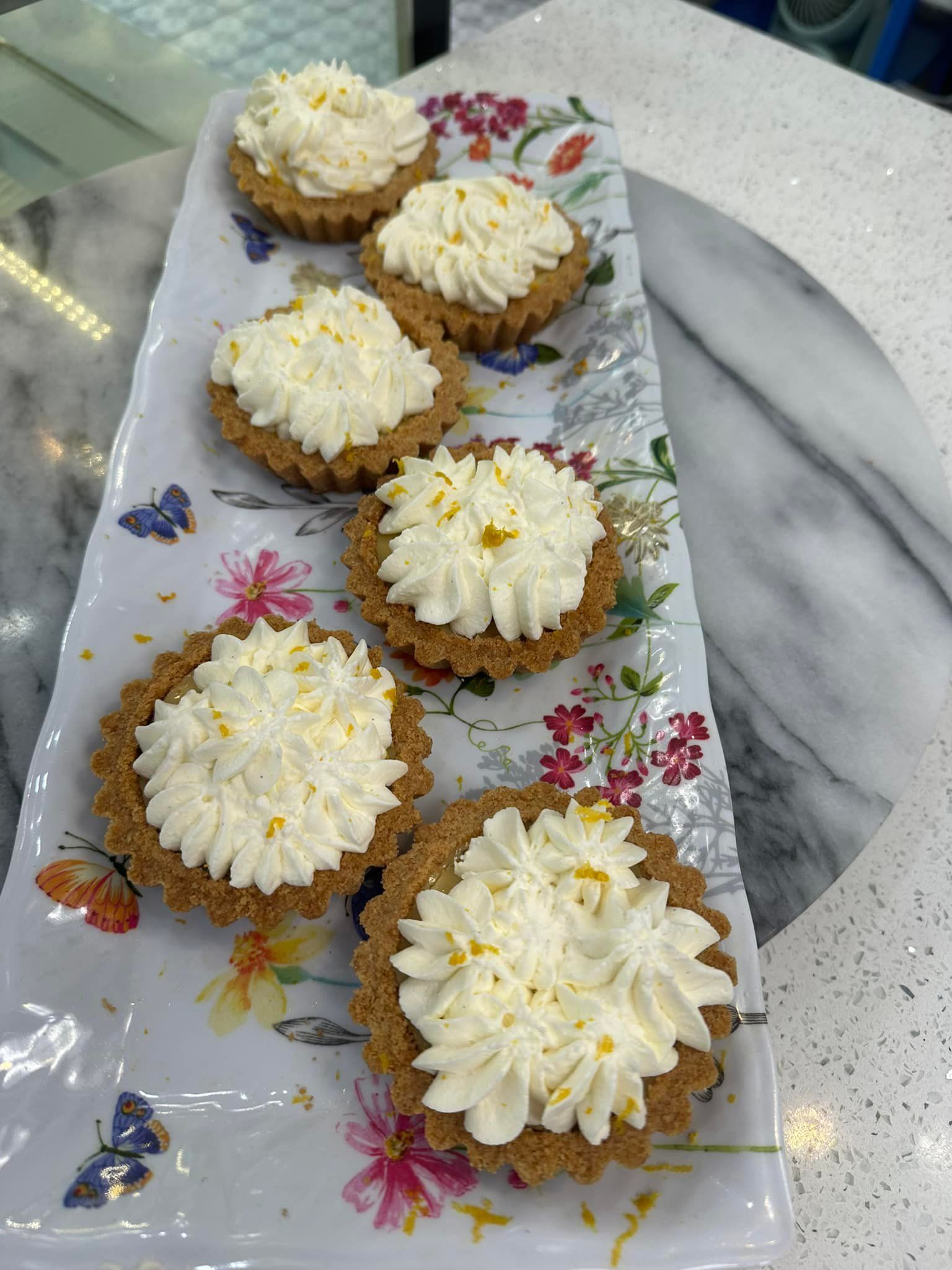 A tray of cupcakes with whipped cream on top on a table.