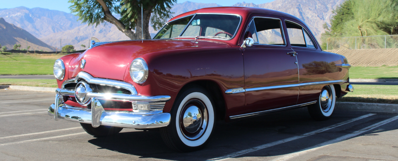 Classic red vintage coupe parked outdoors with mountains in the background.