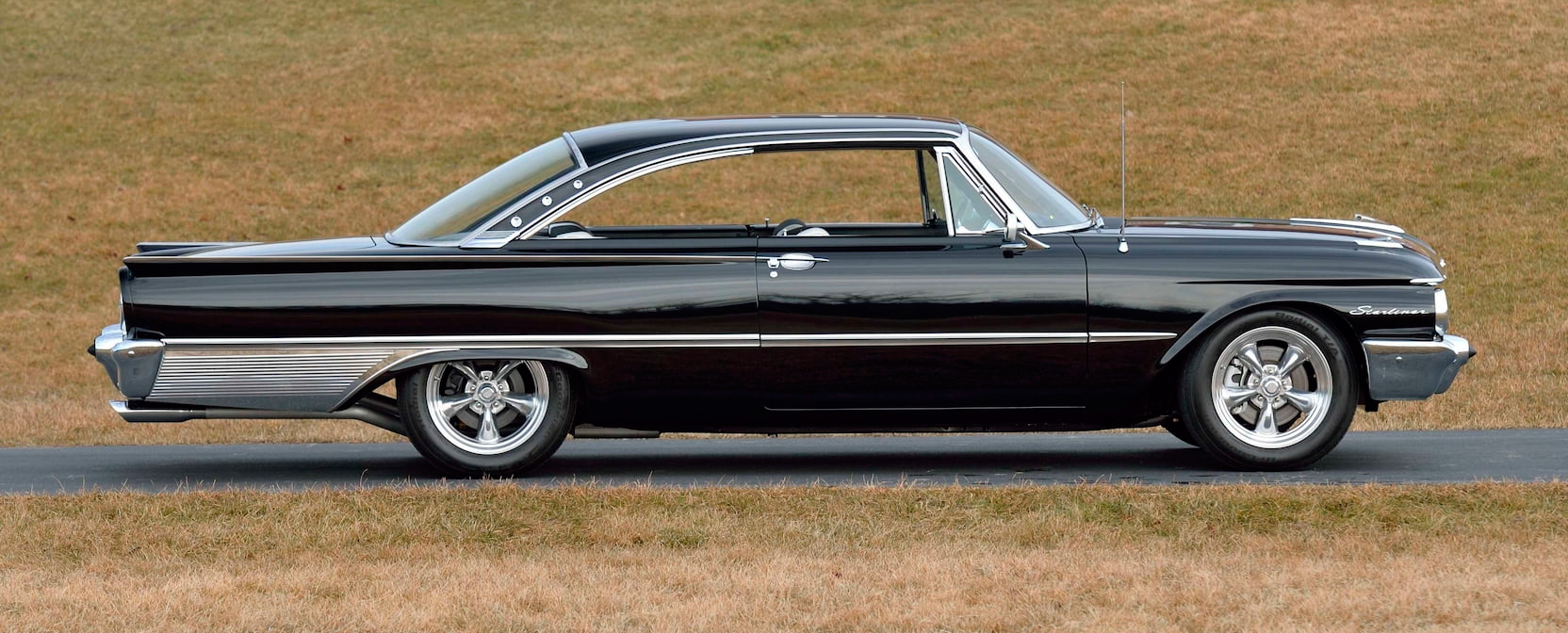 Black classic Galaxie parked on grass, side view with chrome trim and whitewall tires