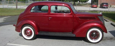 Red vintage Ford coupe with whitewall tires parked outdoors.