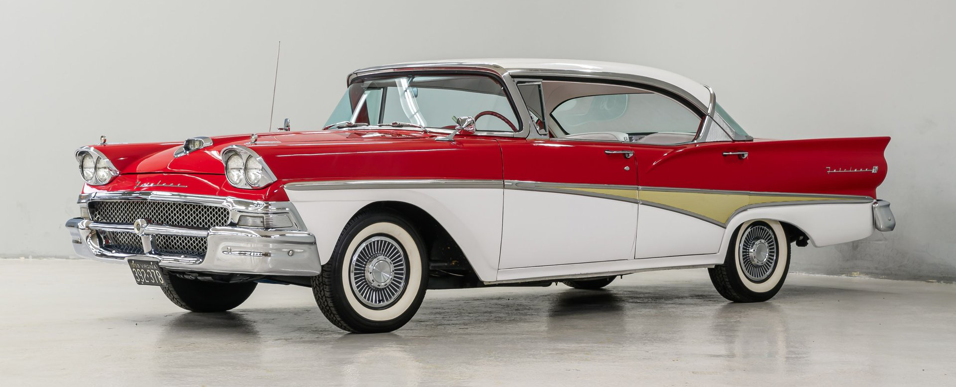 Classic red-and-white 1950s car in a studio setting, side view