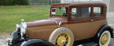 Vintage brown and black Model A coupe with yellow wheels parked on grass