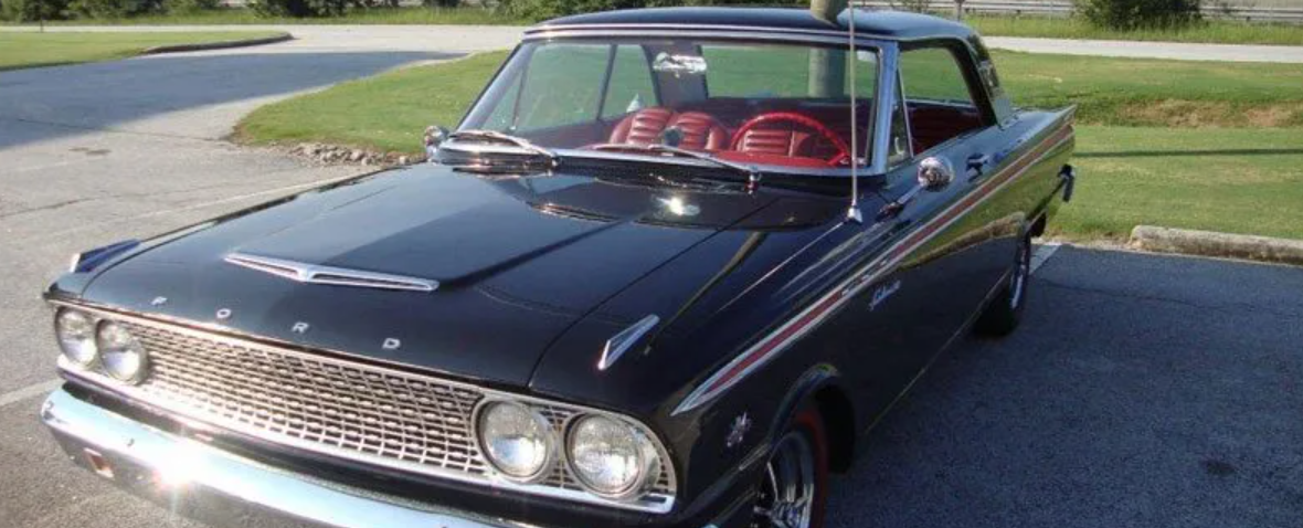 Classic black Fairlane car parked on a driveway, with red interior and chrome grille.