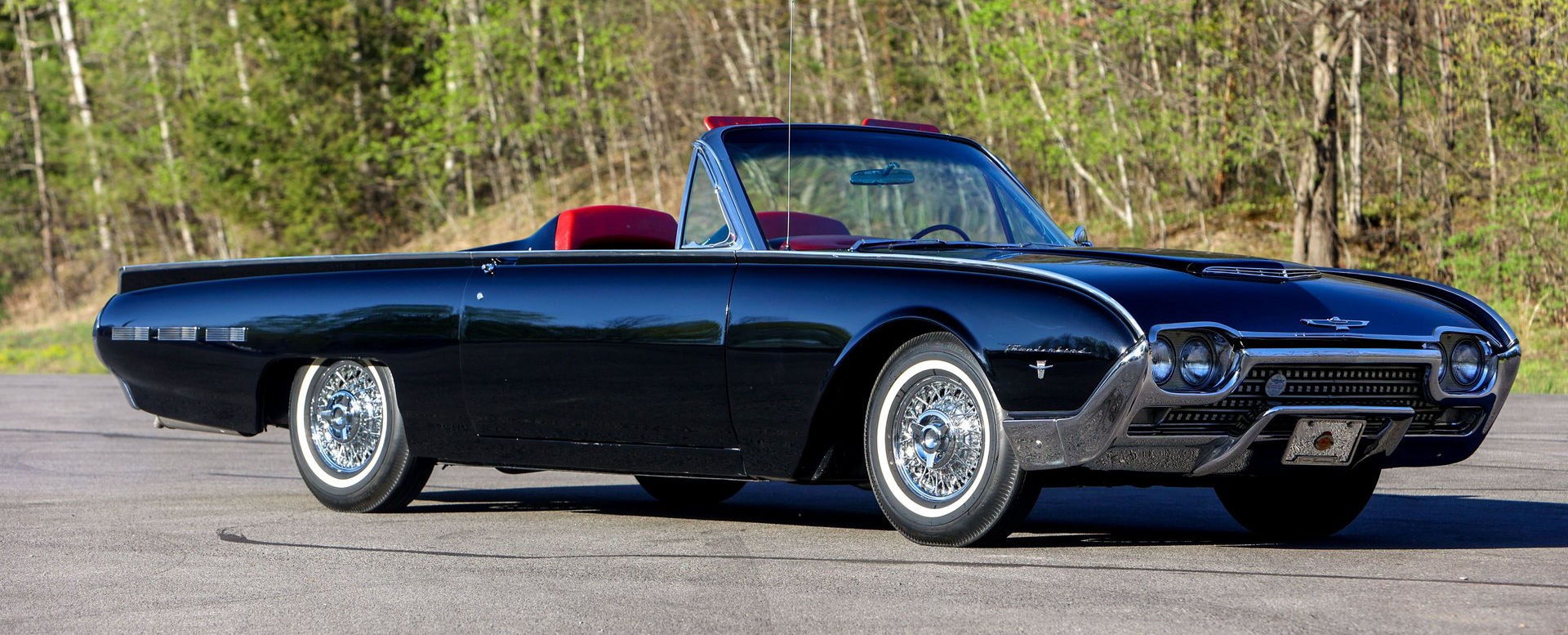 Black classic convertible Thunderbird car with red interior parked outdoors in daylight