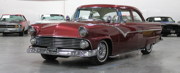 Maroon classic car with chrome details in an indoor showroom, front three-quarter view