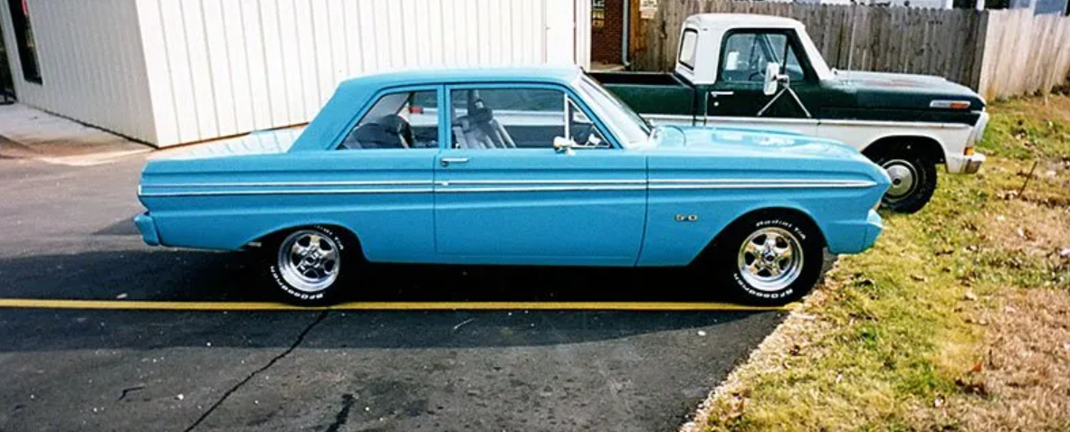Blue classic Falcon coupe parked beside a white pickup truck on a driveway